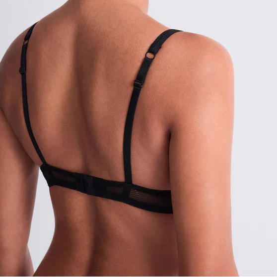 Woman wearing a black bralette against a light gray background