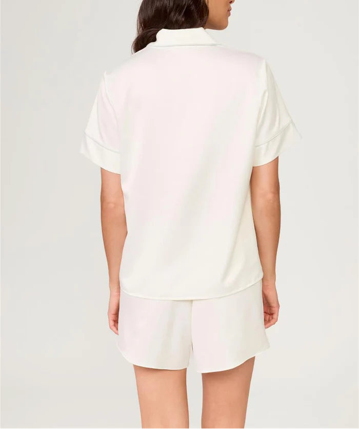 Woman wearing a white polo shirt and shorts on a light gray background