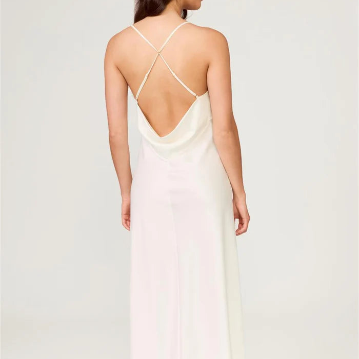 Woman wearing a white slip dress with thin straps on a plain background