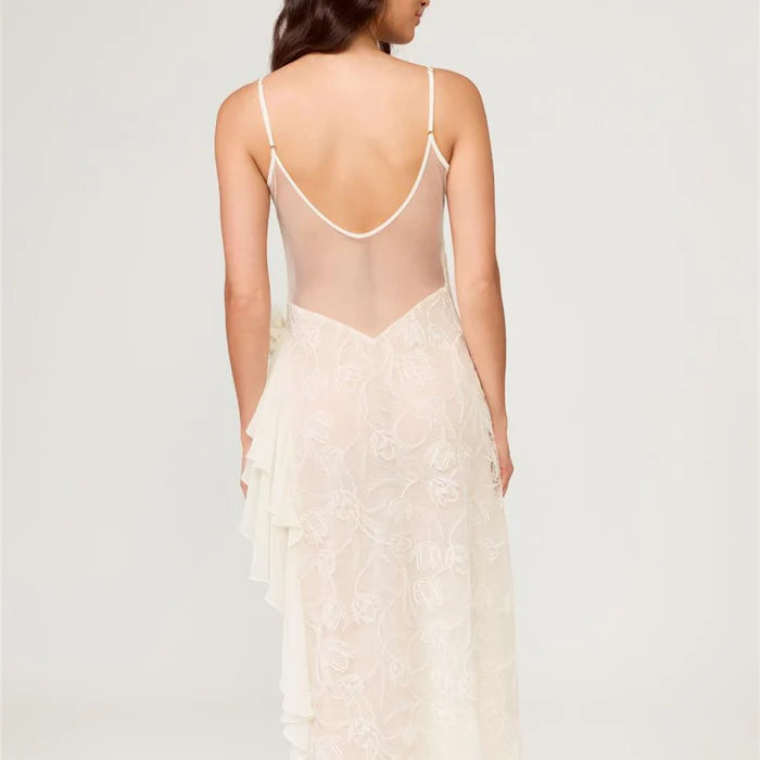 Woman wearing a sheer white lace dress with thin straps on a light gray background