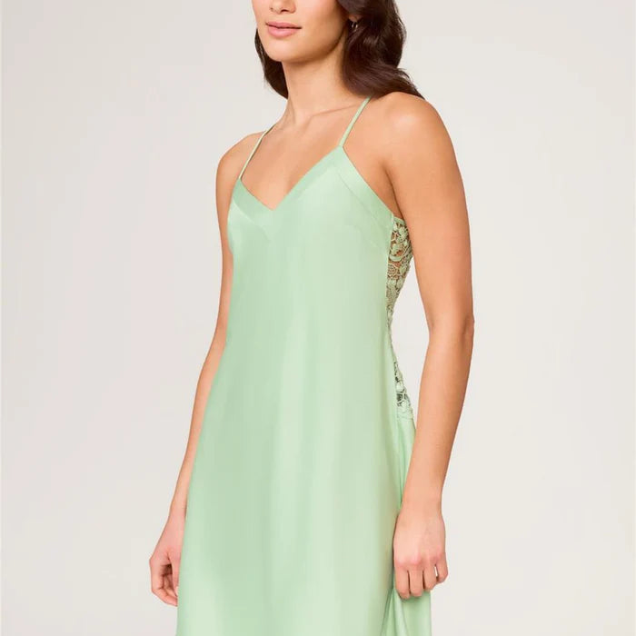 Woman wearing a light green slip dress with lace details on a plain background