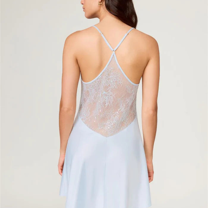 Woman wearing a light blue slip dress with lace detailing on a plain background
