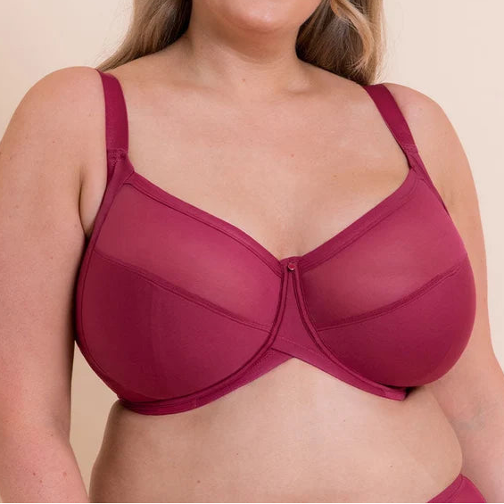 A woman modeling a magenta-colored underwire bra against a solid beige background.