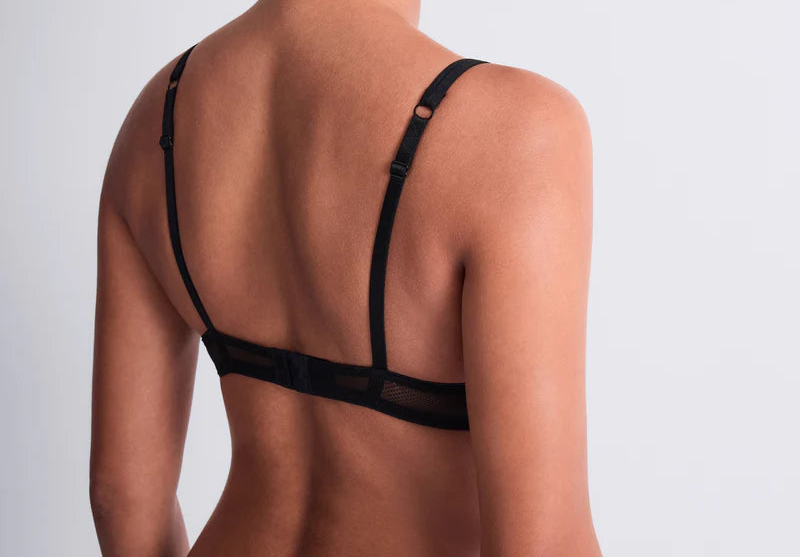 Woman wearing a black bralette against a light gray background