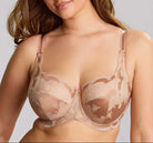 Woman wearing a beige lace bra against a gray background