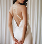 Woman wearing a white wedding dress with a low back against a neutral background
