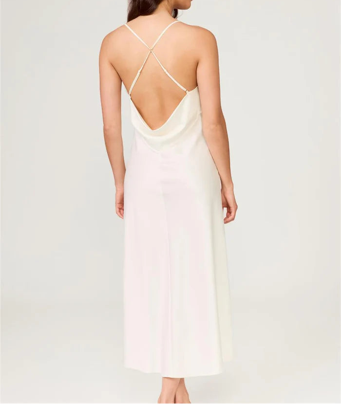 Woman wearing a white slip dress with thin straps on a plain background