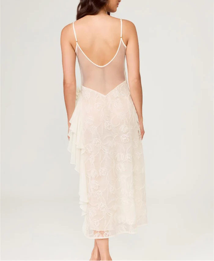 Woman wearing a sheer white lace dress with thin straps on a light gray background