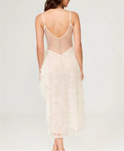 Woman wearing a sheer white lace dress with thin straps on a light gray background