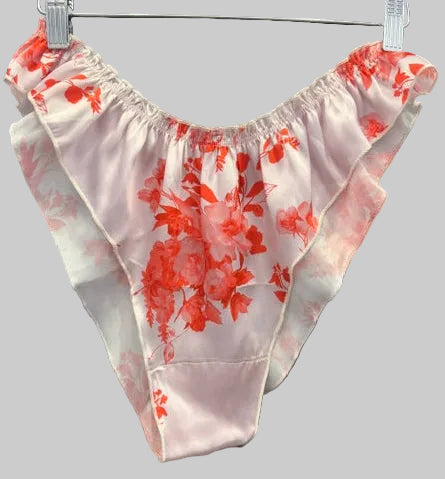 A pair of low-rise, ruffled panties made of light pink satin with a red floral print, hanging on a black hanger against a black satin robe.