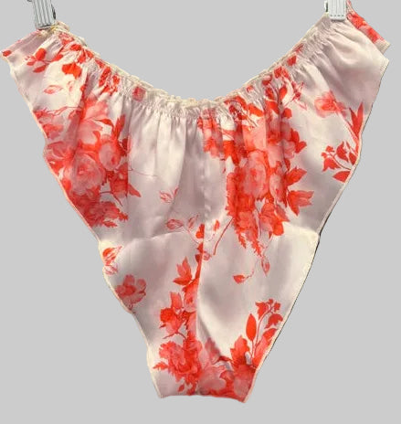 A sheer white satin-like undergarment or lingerie piece with a red floral print, hanging on a black hanger against a black robe backdrop.