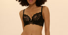 Woman wearing a black lace bra and panties set against a beige background