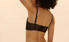 Woman wearing a black bralette against a beige background