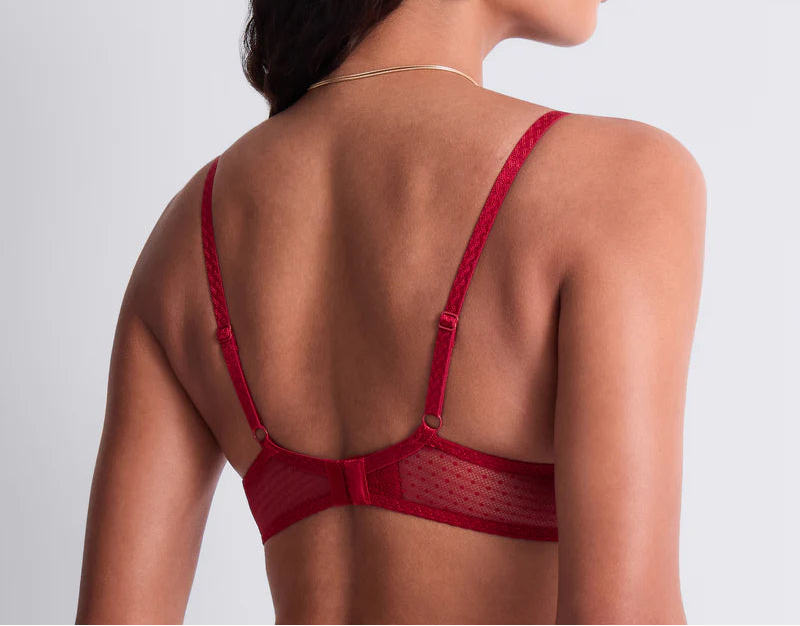 Woman wearing a red bralette with thin straps on a light gray background