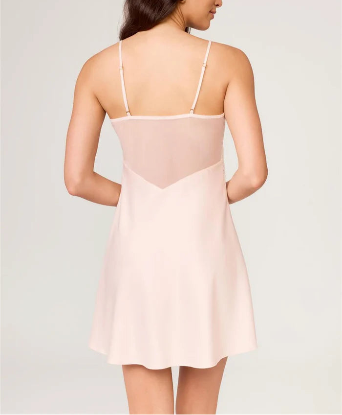 Woman wearing a light pink slip dress against a plain background