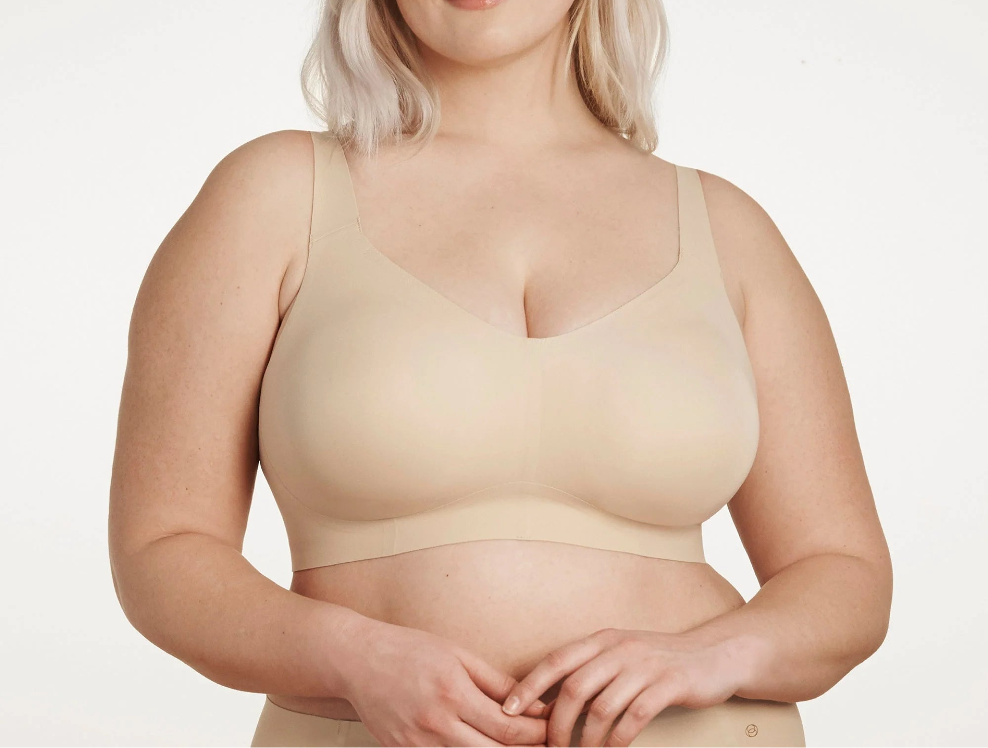 Woman wearing a beige bralette against a plain background