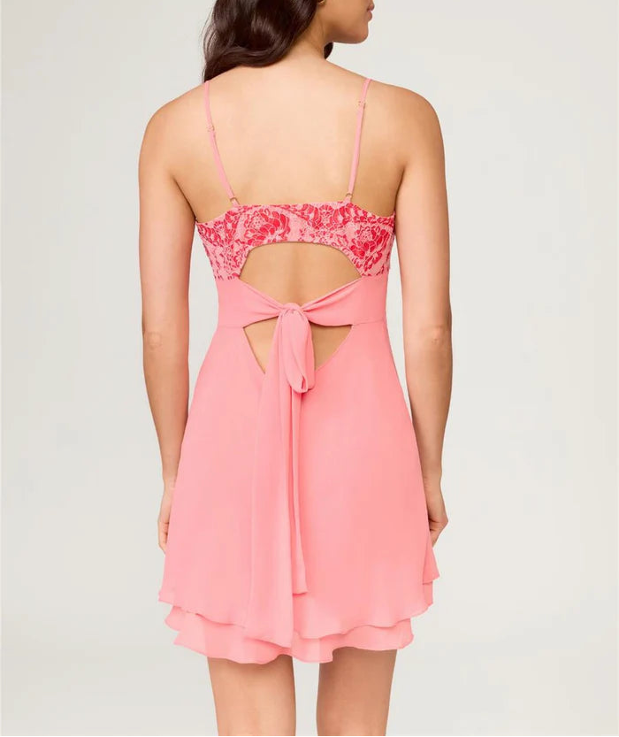 Woman wearing a pink dress with floral lace back on a plain background