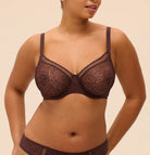 Woman wearing a brown lace bra and panties set against a beige background