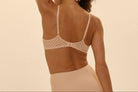 Woman wearing a lace bralette against a beige background