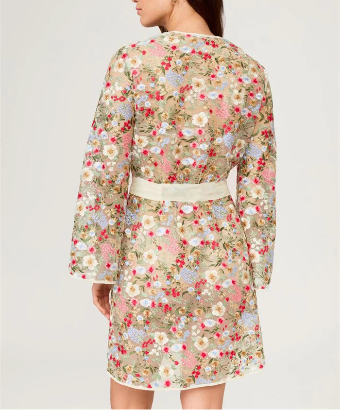 Woman wearing a floral dress with a white belt on a plain background