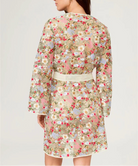 Woman wearing a floral dress with a white belt on a plain background