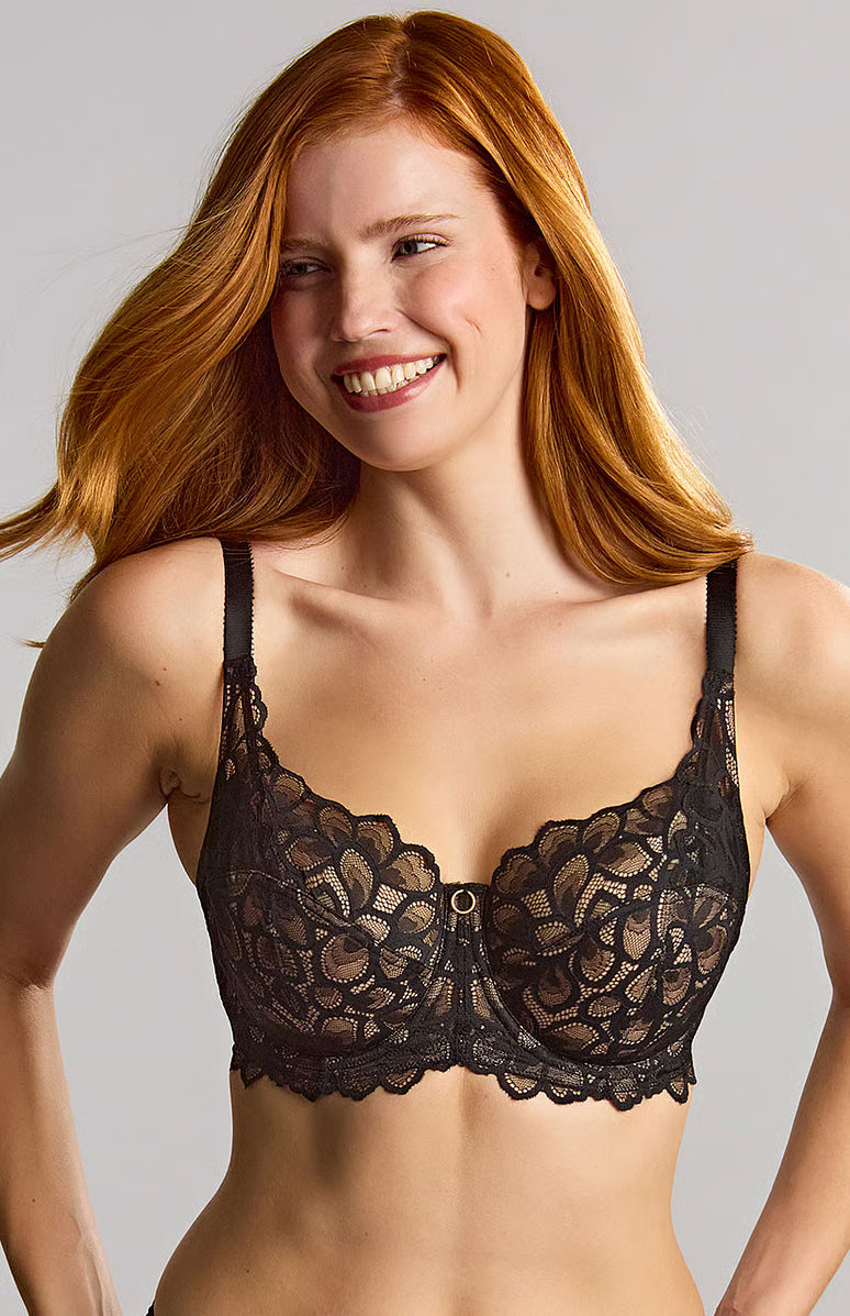 A smiling woman with long red hair wearing a black lace underwire bra against a light gray studio background.