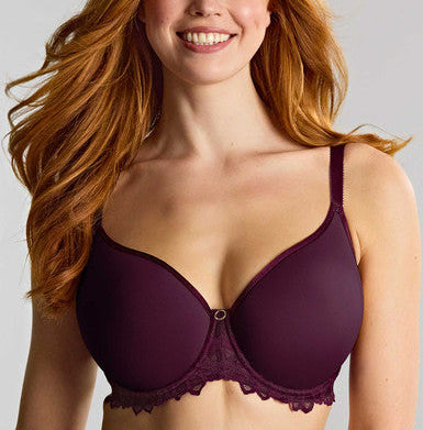 A smiling woman with long wavy red hair wearing a dark plum purple underwire bra with lace trim, photographed against a light gray studio background.