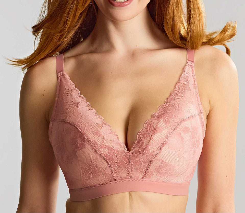 A smiling woman with red hair wearing a dusty pink lace underwire bra against a light gray studio background.