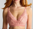 A smiling woman with red hair wearing a dusty pink lace underwire bra against a light gray studio background.