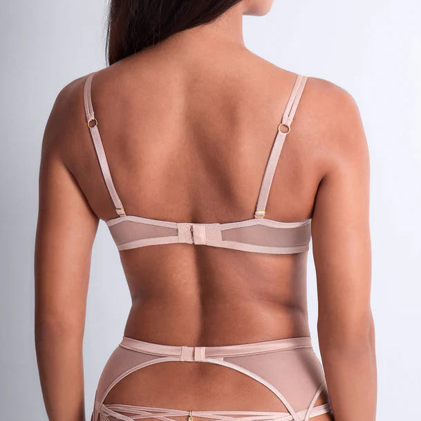 Woman wearing a sheer beige lingerie set on a plain background