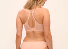 A woman shown from the back wearing a light peach-beige bralette with crossover straps and matching high-cut bikini-style bottoms, against a plain light beige studio background.