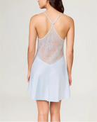 Woman wearing a light blue slip dress with lace detailing on a plain background