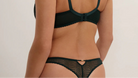 A woman shown from the back wearing a dark forest green bralette and matching sheer lace panties against a plain light background.