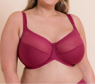 A woman modeling a magenta-colored underwire bra against a solid beige background.